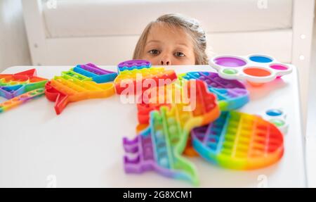 Kleines Mädchen, Kind, Kind spielt mit bunten Pop es Kinderzimmer, Schlafzimmer.Funny trendy Silikon Antistress bunte sensorische Push-Spielzeug popit.Flapping Fi Stockfoto