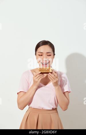 Fröhliche junge asiatische Mädchen hält Stück leckeren Kuchen, lächelnd glücklich auf weißem Hintergrund Stockfoto