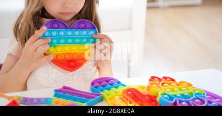 Kleines Mädchen, Kind, Kind spielt mit bunten Pop es Kinderzimmer, Schlafzimmer.Funny trendy Silikon Antistress bunte sensorische Push-Spielzeug popit.Flapping Fi Stockfoto