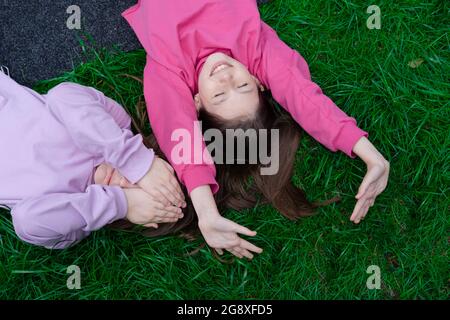 Zwei hübsche Millennial Kids Freunde liegen auf grünem Gras im Park oder Rasen. Kaukasische Mädchen lächeln und Spaß haben zusammen. Von oben. Stockfoto