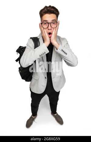 Ein junger Kaukasier, Student in grauer Jacke mit Rucksack isoliert über weißem Studiohintergrund. Volle Länge Stockfoto