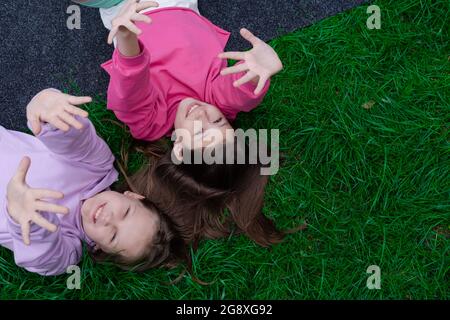 Zwei hübsche Millennial Kids Freunde liegen auf grünem Gras im Park oder Rasen. Kaukasische Mädchen lächeln und Spaß haben zusammen. Von oben. Stockfoto