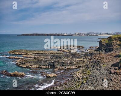 Wellenschliff-Plattform – durch die Wellen erodierte Küstenfelsen – in der Nähe von Portrush an der Antrim Causeway Coast in Nordirland, Großbritannien. Aufgenommen auf einem sonnigen Stockfoto