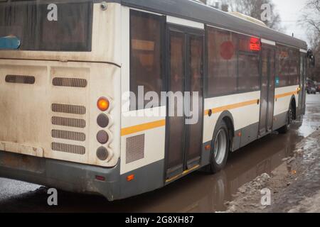 Bus im Winter. Der Transport auf der Straße fährt durch eine Pfütze. Linienbus in Russland. Stockfoto