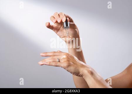 Eine junge Frau, die eine flüssige Pipette verwendet, um ihre Hände mit Hautpflege zu bespreizen. Stockfoto