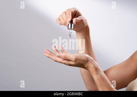 Eine junge Frau, die eine flüssige Pipette verwendet, um ihre Hände mit Hautpflege zu bespreizen. Stockfoto