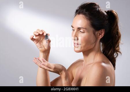 Eine junge Frau, die eine flüssige Pipette verwendet, um ihre Hände mit Hautpflege zu bespreizen. Stockfoto