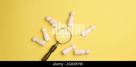 Holzmänner und eine Lupe auf gelbem Hintergrund. Rekrutierungskonzept, Suche nach talentierten und fähigen Mitarbeitern, Karriereentwicklung, Flat Lay Stockfoto