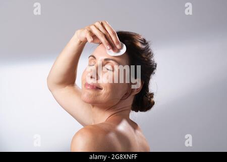 Eine Frau, die ein rundes kosmetisches Wattepad verwendet. Ihre Stirn reinigend. Augen geschlossen. Stockfoto