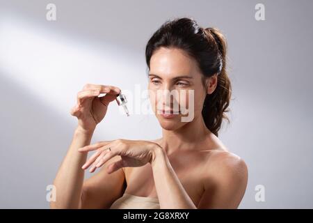 Eine junge Frau, die eine flüssige Pipette verwendet, um ihre Hände mit Hautpflege zu bespreizen. Stockfoto