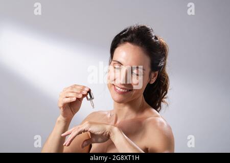 Eine junge Frau, die eine flüssige Pipette verwendet, um ihre Hände mit Hautpflege zu bespreizen. Stockfoto