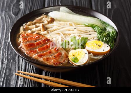 Asiatische Nudelsuppe, Ramen mit Ente, Pilz, Gemüse und Ei in einer Schüssel auf schwarzem Holzgrund. Horizontal Stockfoto