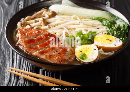 Ramen-Suppe mit Ente, Nudeln, Ei und pak Choi in Schüssel auf schwarzem Tisch aus nächster Nähe. Horizontal Stockfoto