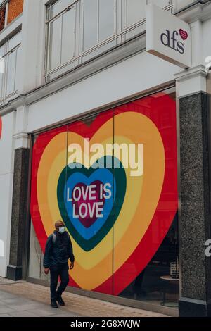 London, Großbritannien - 26. Juni 2021: Mann mit Gesichtsmaske geht am Regenbogenschild „Love is Love Heart“ auf dem Fenster des DFS-Stores in der Oxford Street während des Pride Mon vorbei Stockfoto