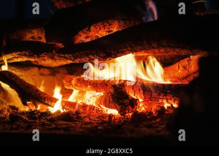 Holz im Feuer mit offenem Feuer und roten Kohlen im Dunkeln Stockfoto