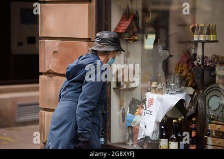 Ältere Frau, die sich das Schaufenster eines Antiquitätenladens anschaut, in dem verschiedene Erinnerungsstücke aus dem Elsass verkauft werden Stockfoto