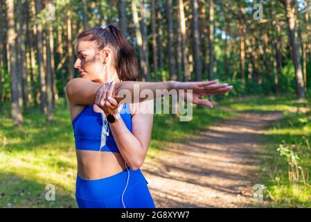 Frau Läuferin streckt die Arme vor dem Training in einem Sommerparkabend. Athletische Frau wärmt Körper vor dem Laufen auf. Kaukasische Weibchen wärmen sich vor Stockfoto