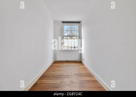 Enger leerer Raum mit weißen Wänden, einem Fenster und einem Holzboden. Stockfoto