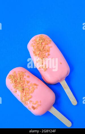Kuchen - Eis in rosa Glasur und Krümel auf blauem Hintergrund. Platz für Text. Eiscreme süßer eskimo mit Schokoladeneisung. Mit Schokolade überzogene Eiskre Stockfoto