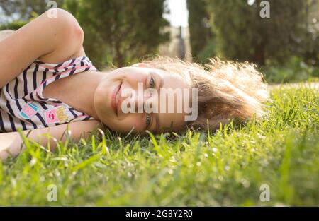 Porträt eines lächelnden Teenagers von 12 Jahren, das an einem sonnigen Tag auf dem Gras liegt. Natur an der frischen Luft genießen, Entspannung, Träume. Fröhlicher Sommer Stockfoto