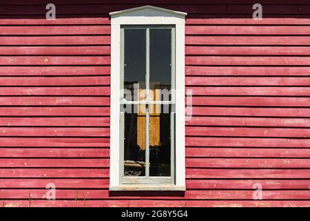 Außenansicht eines alten weiß gestrichenen Fensters auf einem hellroten Klapptafenhaus Stockfoto