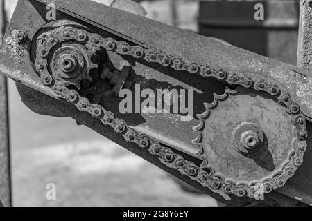 Rostige Details von alten verlassenen Autos. Zahnräder, Ketten, Riemenscheiben rosten im offenen Bereich. Moosbedeckte Metallteile von Landmaschinen. Schwarz-Weiß-Bild Stockfoto