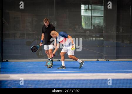 Überwachen Sie den Padel-Unterricht für den Mann, sein Schüler - Trainer lehrt Jungen, wie Padel auf dem Hallentennisplatz zu spielen Stockfoto