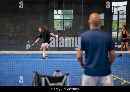 Überwachen Sie den Padel-Unterricht für den Mann, sein Schüler - Trainer lehrt Jungen, wie Padel auf dem Hallentennisplatz zu spielen Stockfoto