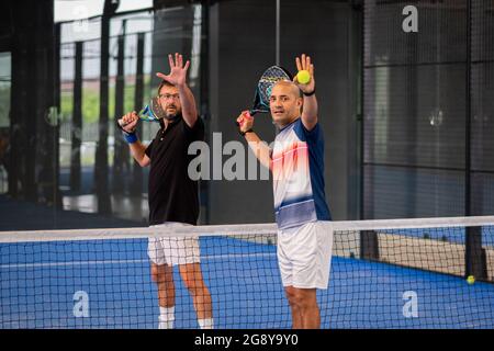 Überwachen Sie den Padel-Unterricht für den Mann, sein Schüler - Trainer lehrt Jungen, wie Padel auf dem Hallentennisplatz zu spielen Stockfoto