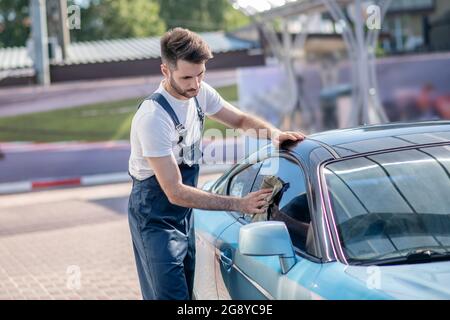 Junger bärtiger Mann, der Autoglas abwischt Stockfoto