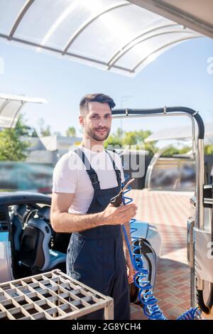 Fröhlicher Mann im Overall beim Autoservice im Freien Stockfoto