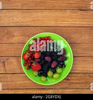 Beerenmischung - Johannisbeeren, Stachelbeeren, Maulbeeren, Erdbeeren in einem Teller auf einem hölzernen Hintergrund mit Kopierfläche. Sommerkonzept. Stockfoto