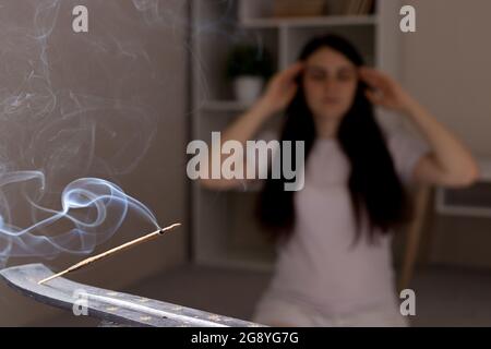 Ein aromatischer Indianerstab brennt, die Frau im Hintergrund meditiert. Aromatherapie, Selbsteintauchen, die Kraft des Denkens Stockfoto