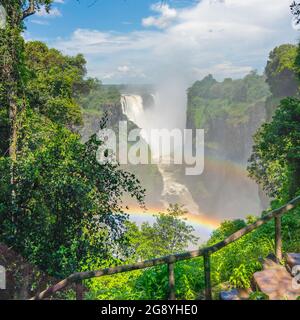 Regenbogen überVictoria Falls am Zambezi Fluss, Grenze von Sambia und Simbabwe mit blauem Himmel Stockfoto