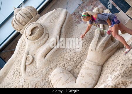 Prora, Deutschland. Juli 2021. Eine Frau arbeitet auf dem Gelände des Sandskulpturen-Festivals auf Rügen an einer großen Sandfigur aus dem Märchen 'Froschprinz'. Für die Sandskulpturen-Schau, die am 24.07.2021 für die Öffentlichkeit zugänglich sein wird, kreieren derzeit Künstler aus verschiedenen europäischen Ländern im Ostseebad Binz 45 Riesenfiguren. Quelle: Stefan Sauer/dpa/Alamy Live News Stockfoto