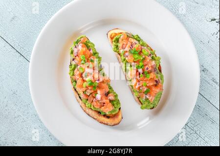 Zwei Guacamole und Lachs Toasts auf weißem Teller Stockfoto