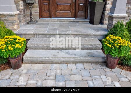 Auf der ursprünglichen Betonverande aufgetragene Steinplatten, Stufen aus Naturstein und eine gestürzte Fertigerlandung sorgen für ein frisches Landschaftsupdate. Stockfoto