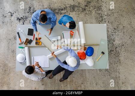 Eine Gruppe von vier Personen, darunter Ingenieur und Geschäftsleute, diskutieren und besprechen Baumaterial aus der Vogelperspektive aus dem oberen Winkel Stockfoto