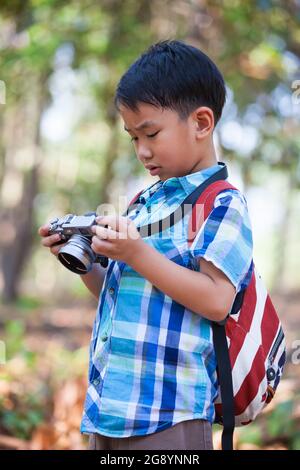 Asian smart boy Überprüfung und Überprüfung von Fotos in professionellen Digitalkamera über Natur Hintergrund. Aktiver Lebensstil, Neugier, ein Hobby verfolgen, te Stockfoto