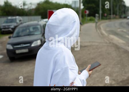 Teenager-Mädchen in weißer Kapuze. Er läuft herum. Ein modernes Kind in der Stadt. Ein Mädchen in einer Kapuzenmütze. Stockfoto