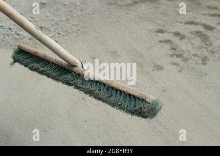 Der Mopp entfernt Staub und Sand von der Straße. Außenreinigungsreiniger. Ein Wischmopp mit festen Borsten und einem Griff aus Holz. Stockfoto