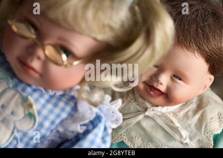 Nahaufnahme einer Vintage-Baby-Puppe, die mit einer Brille über die Mädchen-Puppe lacht. Stockfoto