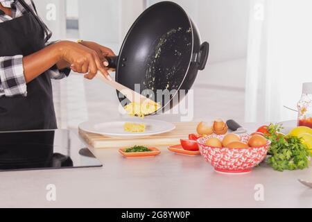 Rühreier, die aus einer tiefen Bratpfanne auf einen Teller gegossen wurden Stockfoto