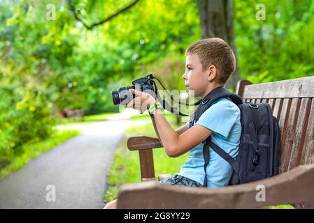 Tourist mit einer Kamera. Ein Junge mit Kamera fotografiert die Natur im Park. Ein junger Fotograf sitzt auf einer Parkbank und fotografiert Stockfoto