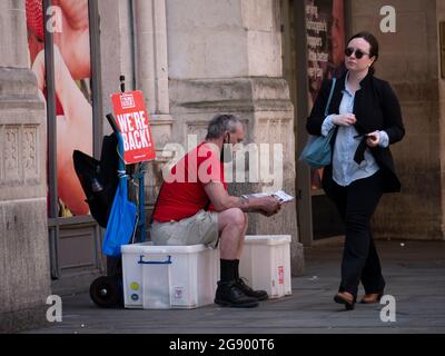 Big Issue Seller with We're Back Sign in Bishopsgate London, während der Covid-19, Covid, der Coronavirus-Pandemie, ist The Big Issue eines der führenden Sozialunternehmen Großbritanniens und hilft Obdachlosen oder Menschen, die von Obdachlosigkeit bedroht sind, die Möglichkeit, einen Lohn zu verdienen Stockfoto