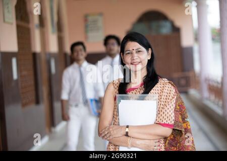 Selbstbewusst lächelnde indische Lehrerin mit Schülern im Hintergrund Stockfoto