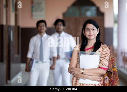 Selbstbewusst lächelnde indische Lehrerin mit Schülern im Hintergrund Stockfoto