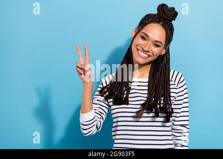 Foto-Porträt eines lächelnden Mädchen mit Dreadlocks Top-Knoten tragen gestreiftes Hemd mit V-Zeichen Geste isoliert pastellblau Hintergrund Stockfoto