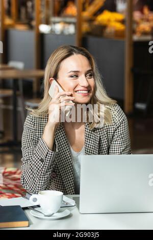 Lächelnde Geschäftsfrau schaut weg, während sie im Café mit dem Mobiltelefon spricht Stockfoto