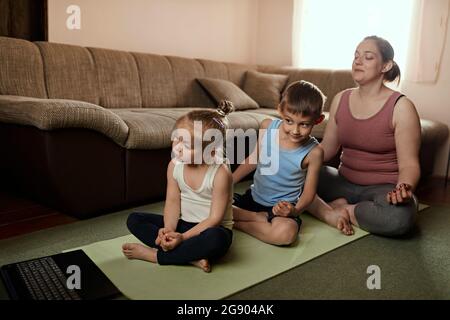 Mutter macht Yoga mit Sohn und Tochter, während sie sich das Online-Tutorial über den Laptop ansieht Stockfoto